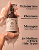 A bottle of Able & Mane Hydrating Shampoo being washed with soapy hands, set against a warm beige background with promotional text highlighting moisturizing, cleansing, and scalp benefits.
