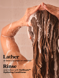 A person with long, wet brown hair lathered in foam, shown from the back while washing. Text on the left reads, 'Lather at least 3 pumps on wet hair Rinse and follow with HoliRoots™ Hydrating Conditioner.